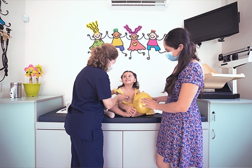 Bewegung bei Krebs: Kind sitzt auf der Liege, vor ihr stehen die Mutter und die Ärztin